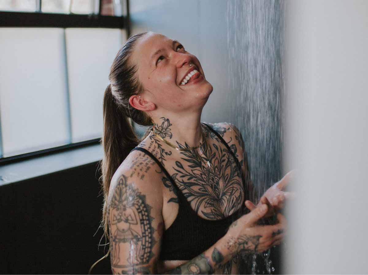 Woman with beautiful tattoos rinsing off in a cold shower at Sauna House Asheville.