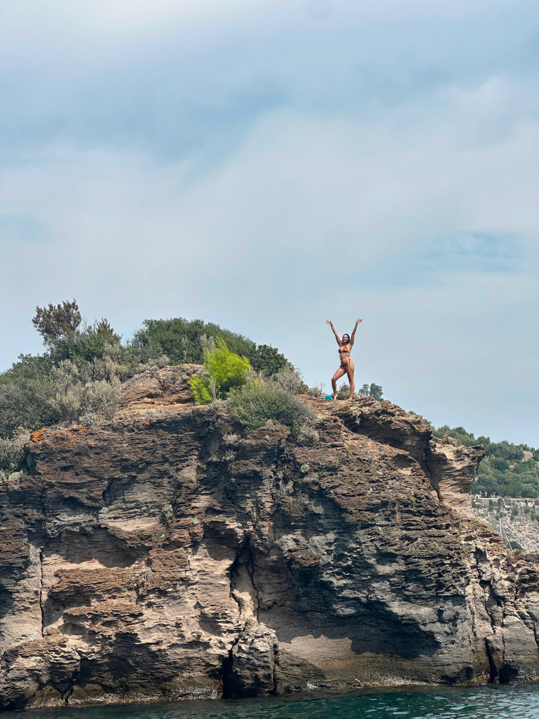 Person standing on the edge of a rocky coastal cliff in Italy