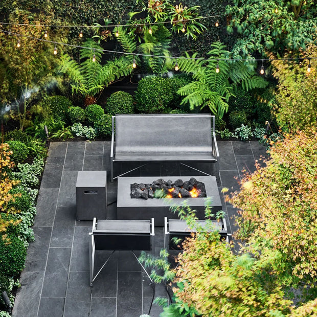 Two Evia Chairs and an Evia Lounge around a fire pit on a porch surrounded by greenery