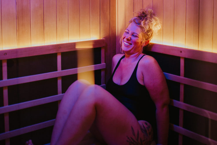 Person sitting in a private infrared sauna cabin with red and purple light, smiling