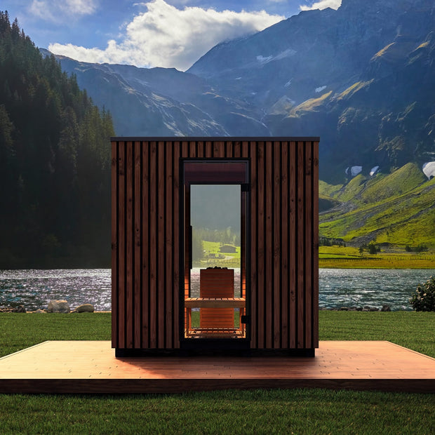 Garda sauna next to a lake and beautiful mountain range. You can see through both sets of windows of the sauna to see the landscape on the other side